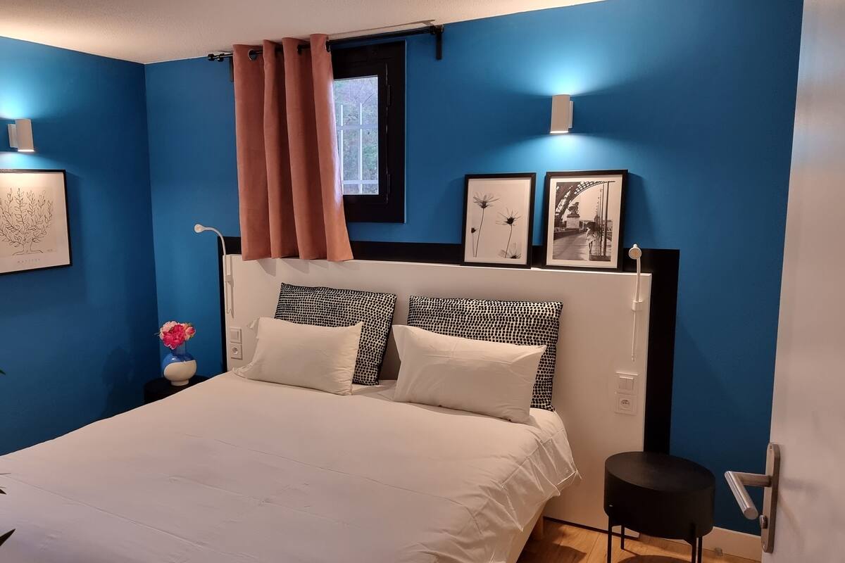 Ein Schlafzimmer mit einem Bett, einem Nachttisch, einer Vase mit Blumen und Wandleuchten.