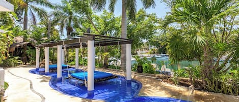 A pool area with a wooden pergola, palm trees, and a clear blue pool.