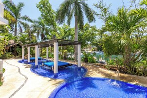Un área de piscina con una pérgola de madera, palmeras y una piscina azul cristalina.