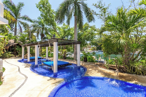 A pool area with a wooden pergola, palm trees, and a clear blue pool. - Aventuras Club (Puerto Aventuras)
