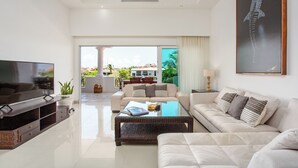 A modern living room with a flat-screen TV, a glass coffee table, and a beige sofa. - Aventuras Club (Puerto Aventuras)