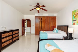 Una habitación de hotel con dos camas, un ventilador de techo, un armario de madera, una mesita de noche y un cuadro en la pared.