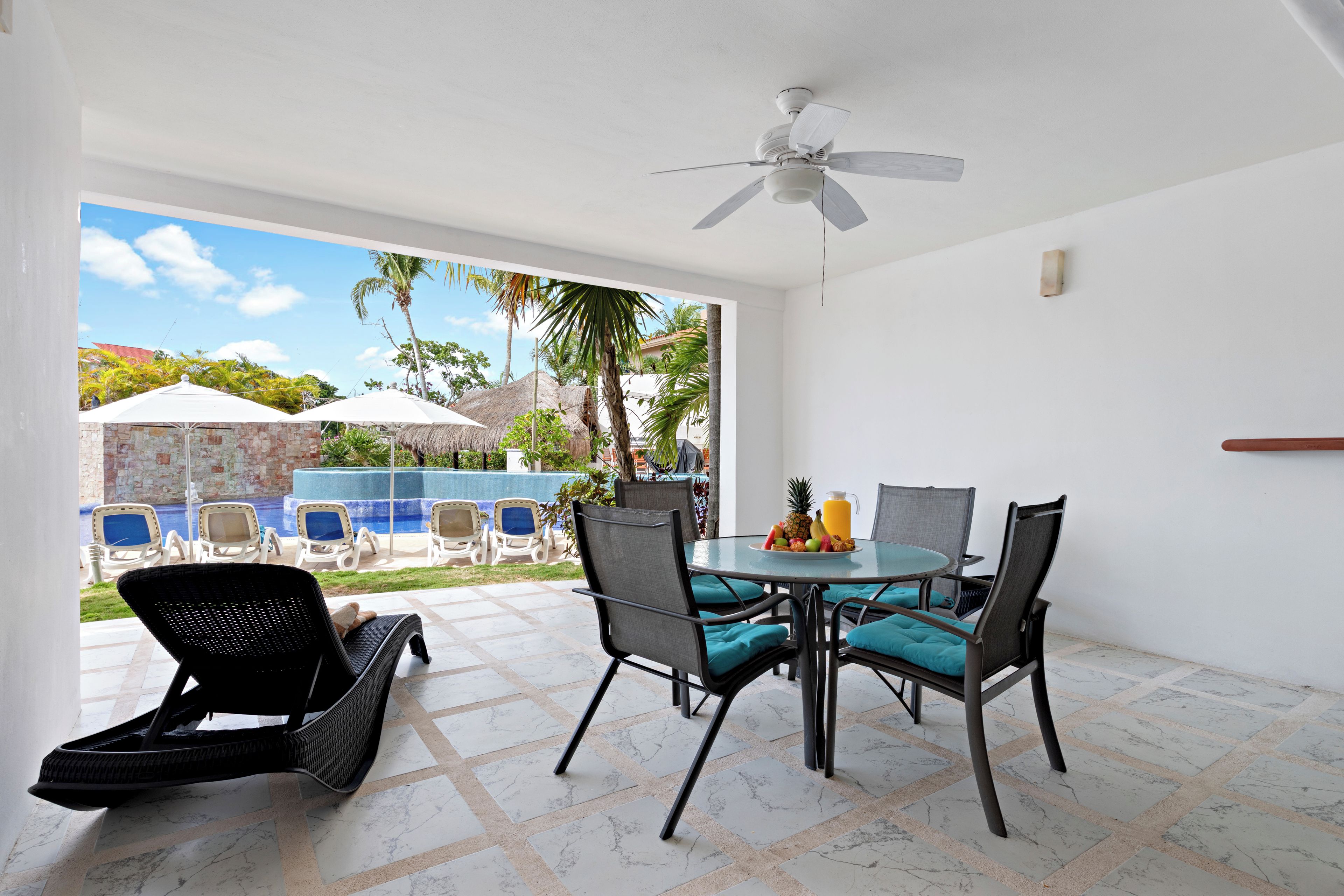A dining area with a table and chairs, a ceiling fan, and a view of a swimming pool and palm trees.