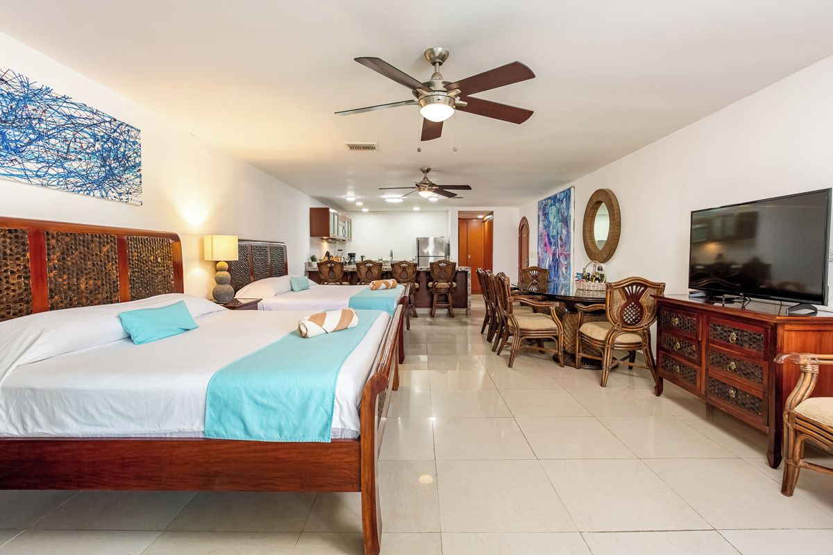 A hotel room with two beds, a dining area, a TV, and a ceiling fan.