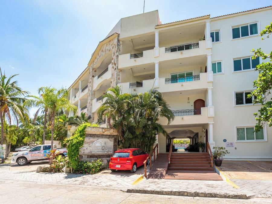 Un edificio de varios pisos con entrada central, balcones y un estacionamiento con automóviles.