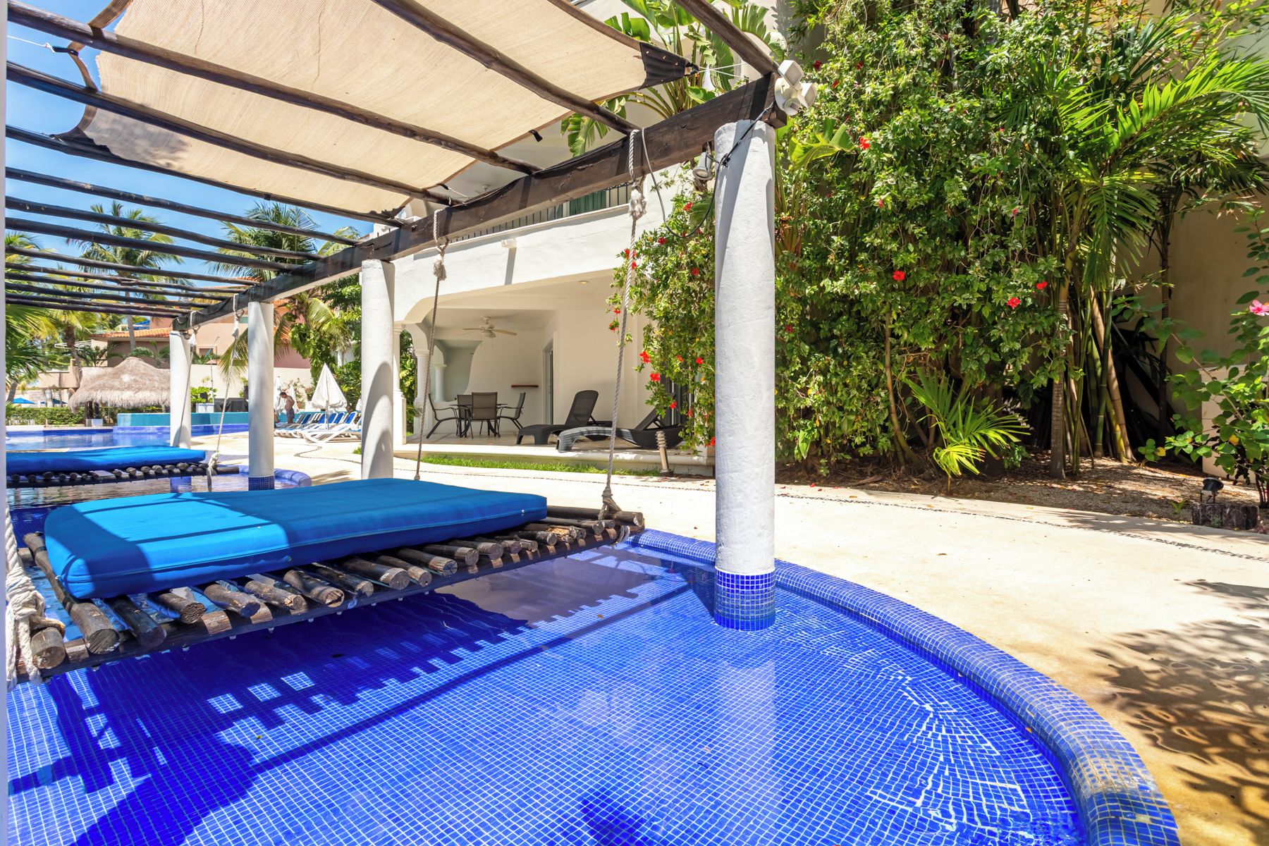 Area piscina con pavimento piastrellato blu, sedie a sdraio e una zona relax coperta.