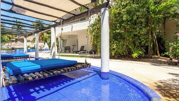 A pool area with blue tiled flooring, lounge chairs, and a covered seating area.