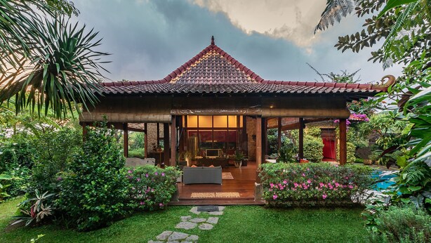 A traditional-style building with a tiled roof, surrounded by lush greenery and a stone pathway leading to a seating area. - Villa Mulyono (Batu)