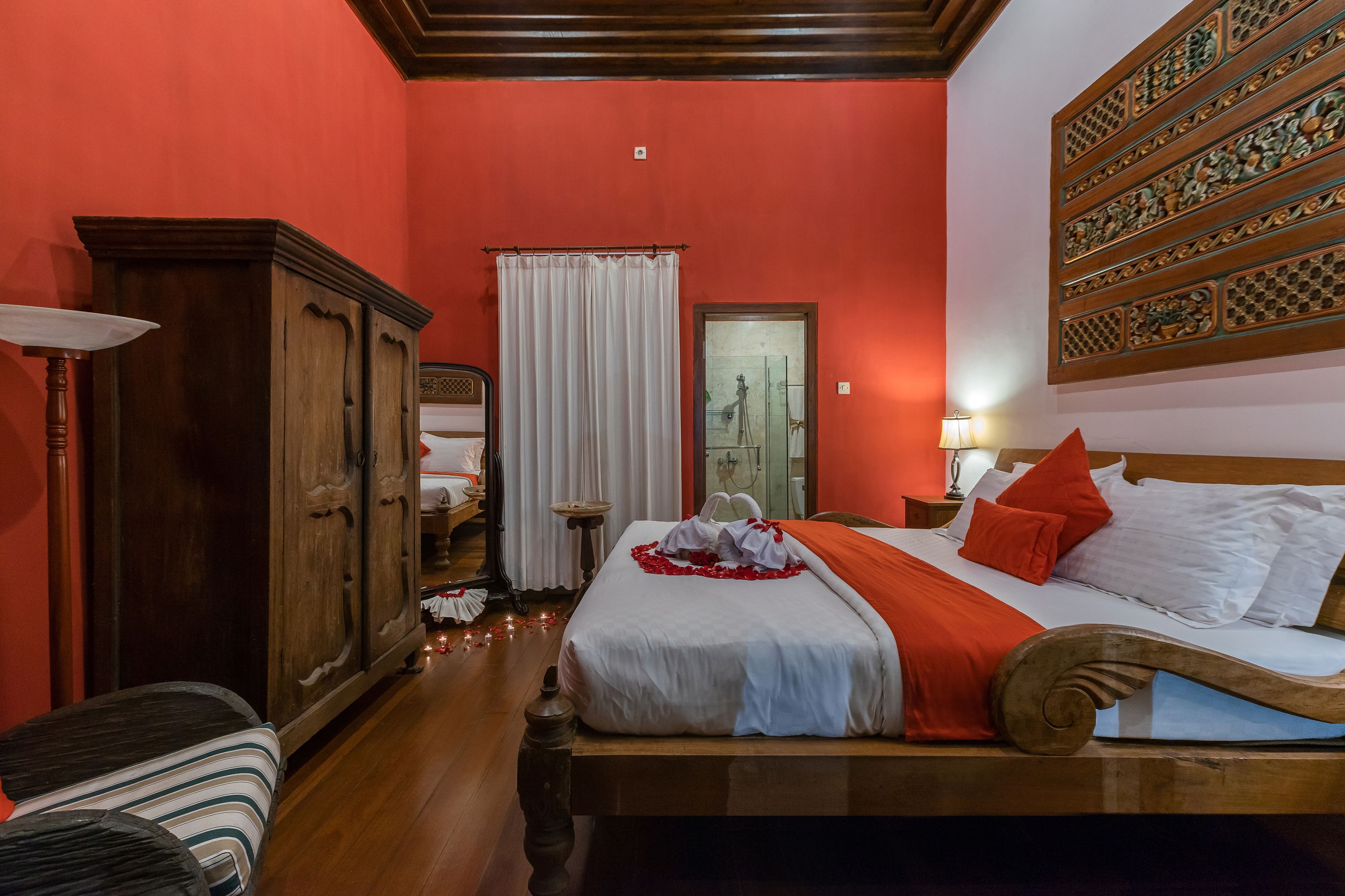 A hotel room with a wooden bed, a wardrobe, a bathroom with a shower, and a decorative wall panel.