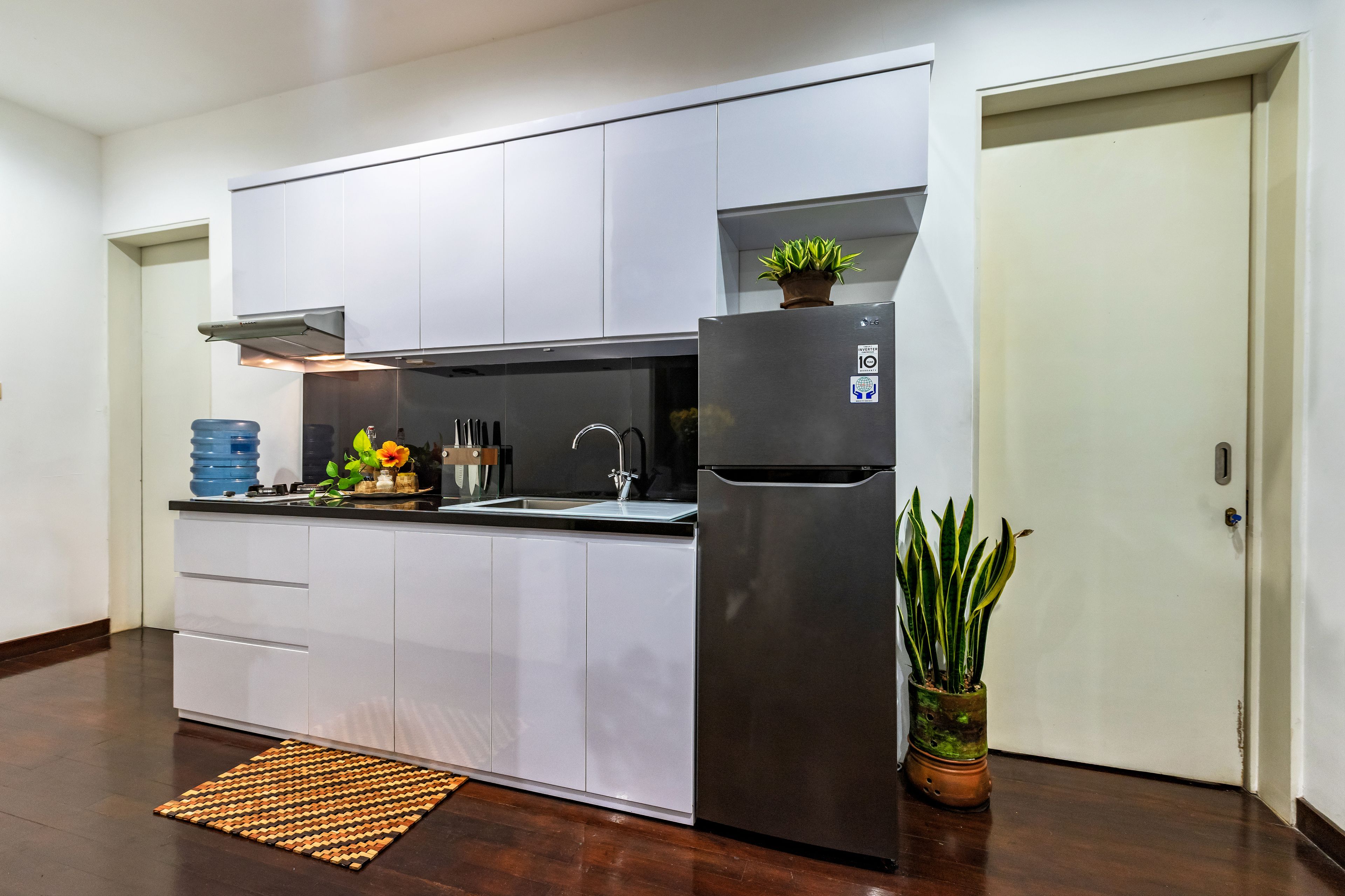 A modern kitchen with white cabinets, a stainless steel refrigerator, and a potted plant.