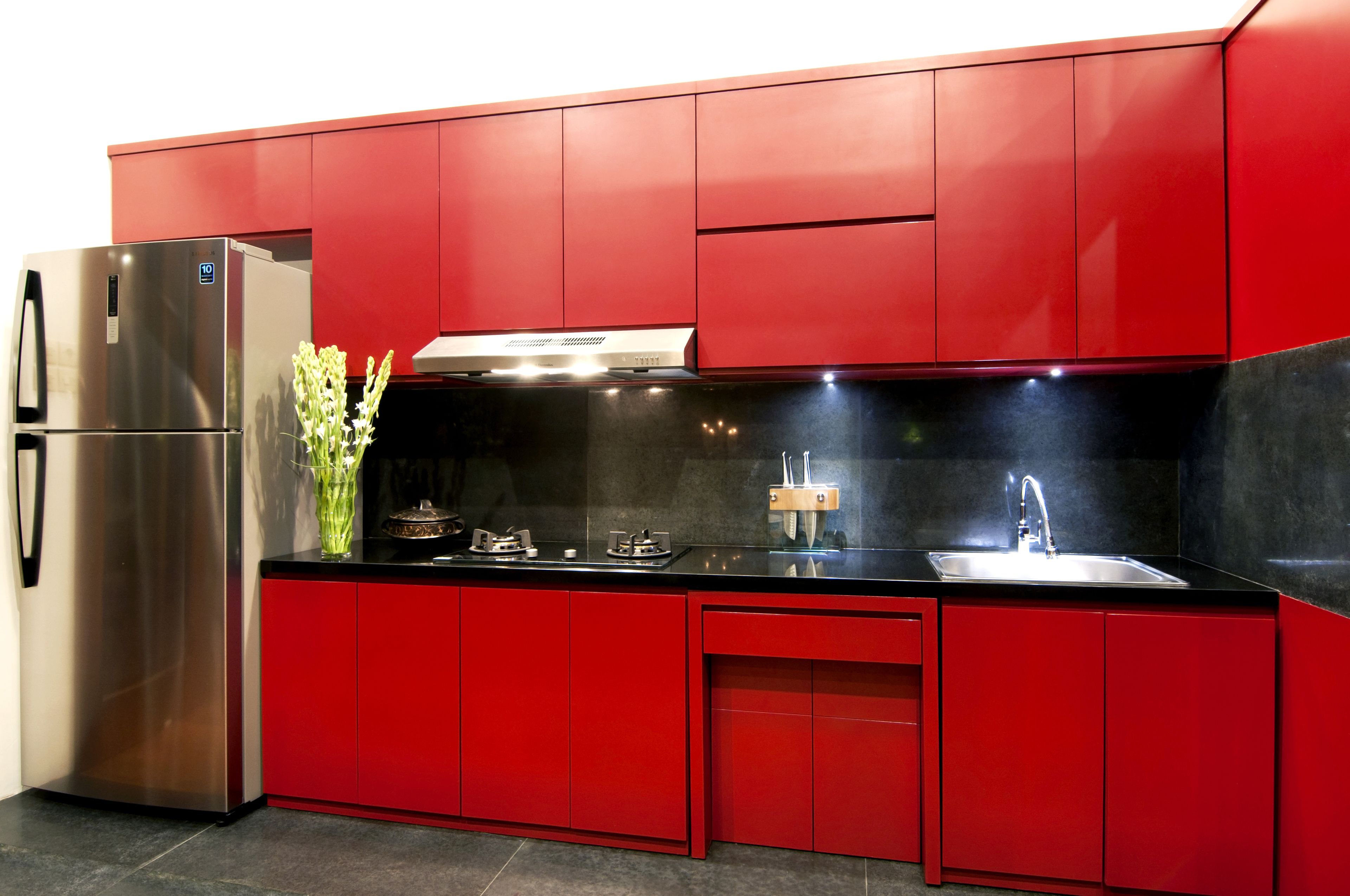 A modern kitchen with red cabinetry, a stainless steel refrigerator, a gas stove, and a sink.