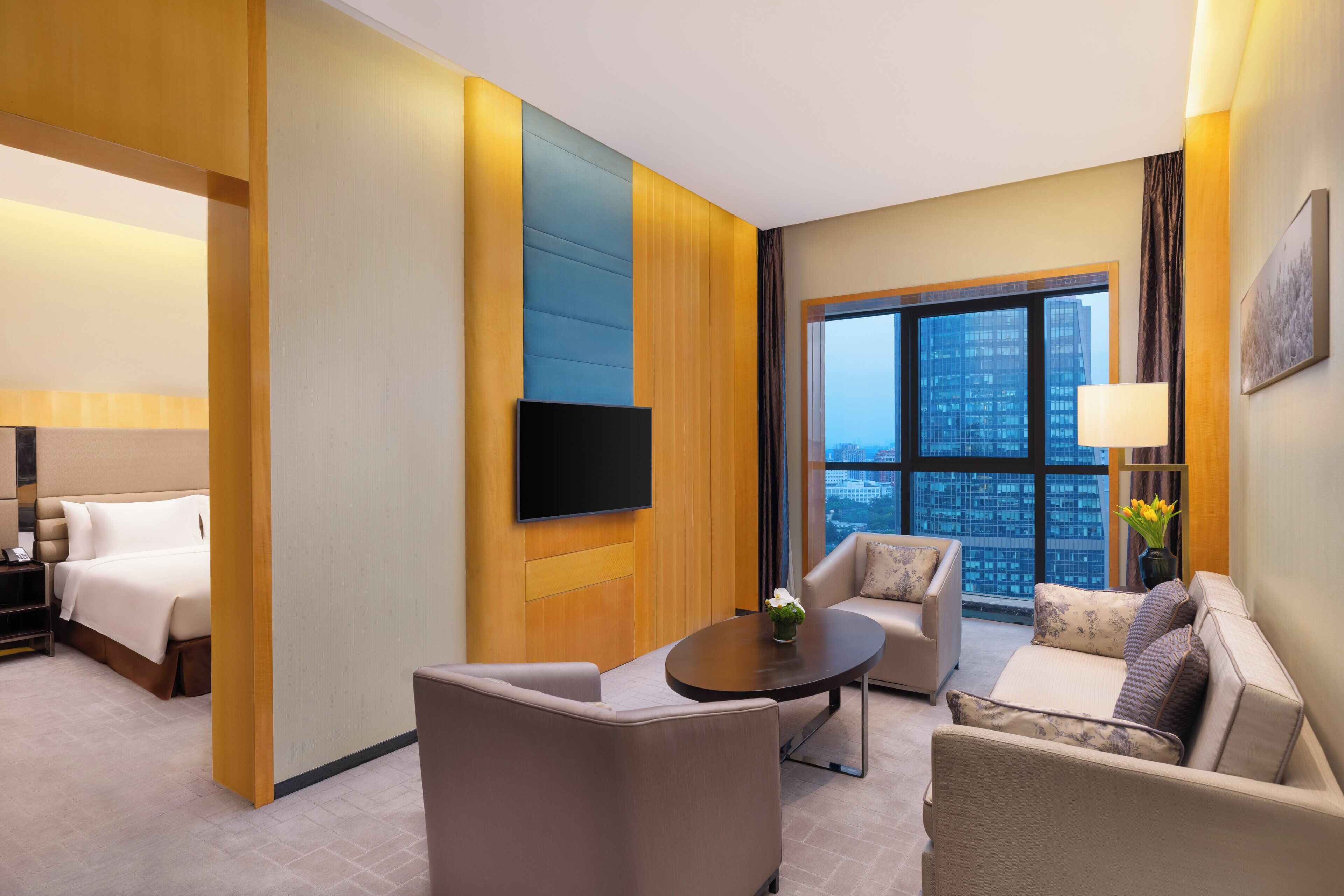 Une chambre d’hôtel moderne dotée d’un lit, d’un coin salon avec une table basse et d’une grande fenêtre donnant sur la ville.