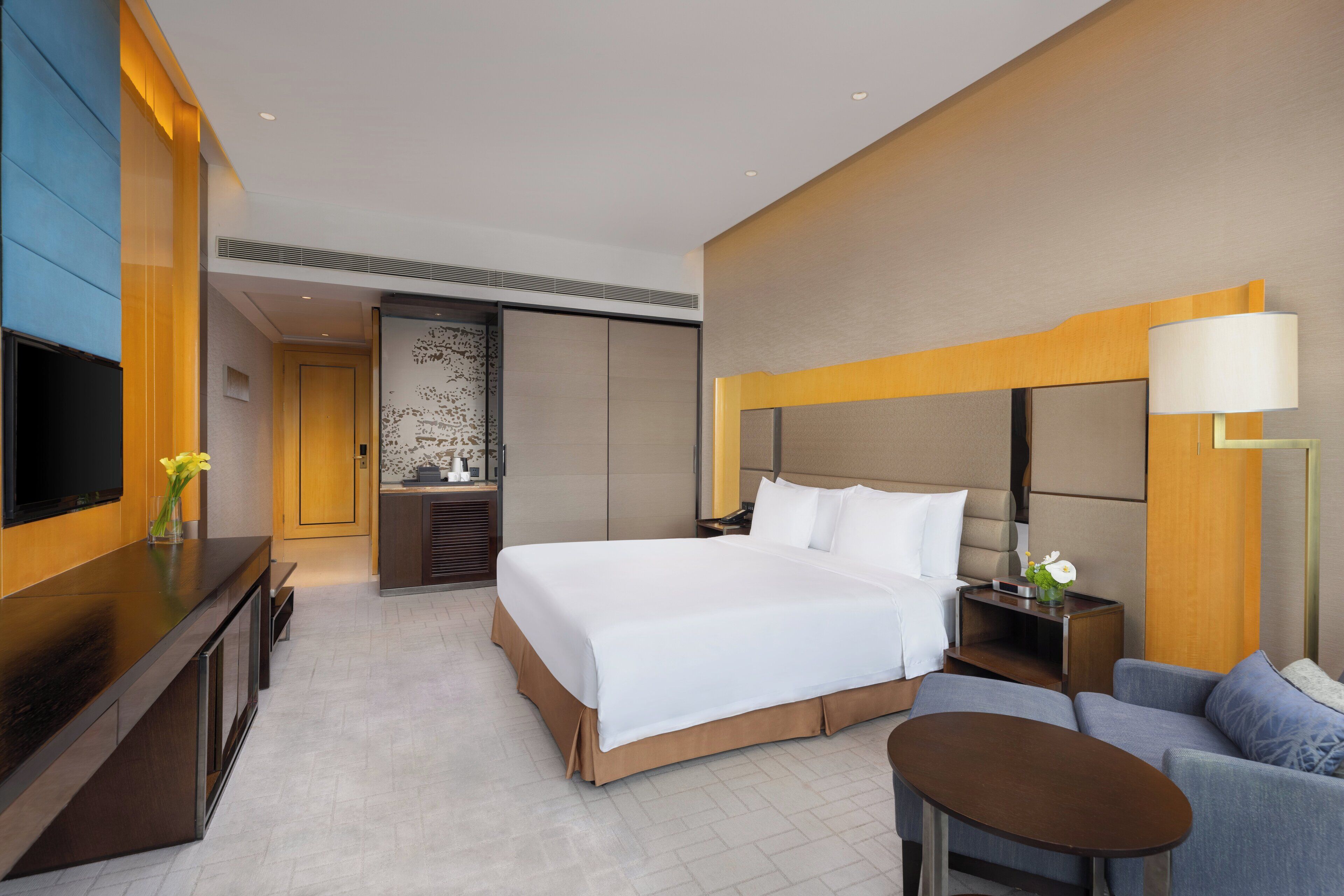 A modern hotel room with a large bed, a TV, a desk, and a sofa.