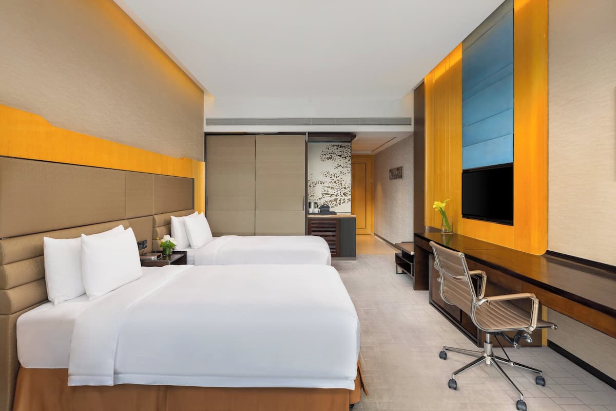 Une chambre d’hôtel avec deux lits, un bureau, une chaise et un téléviseur fixé au mur.