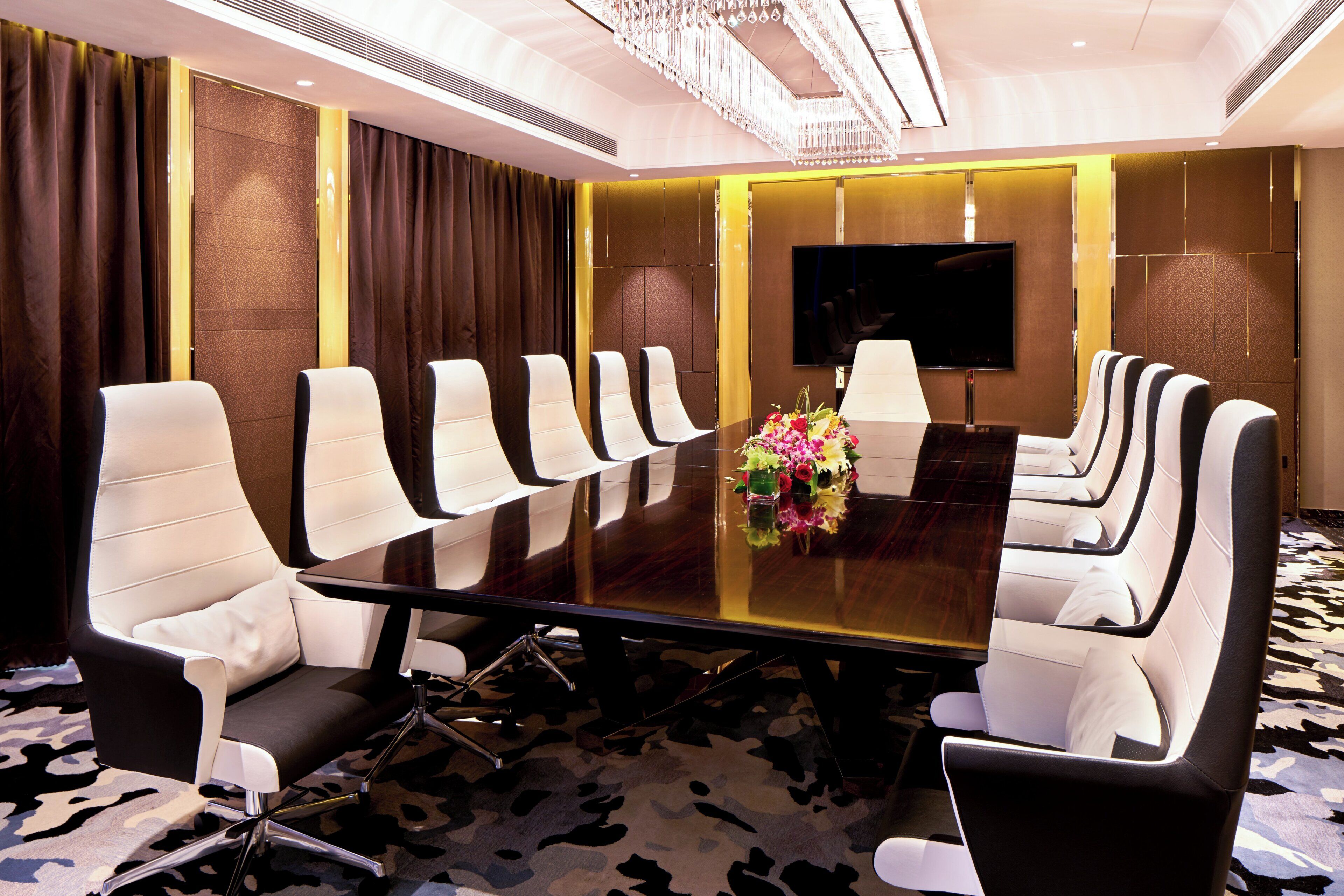 A conference room with a long table, multiple chairs, a TV screen, and a floral centerpiece.