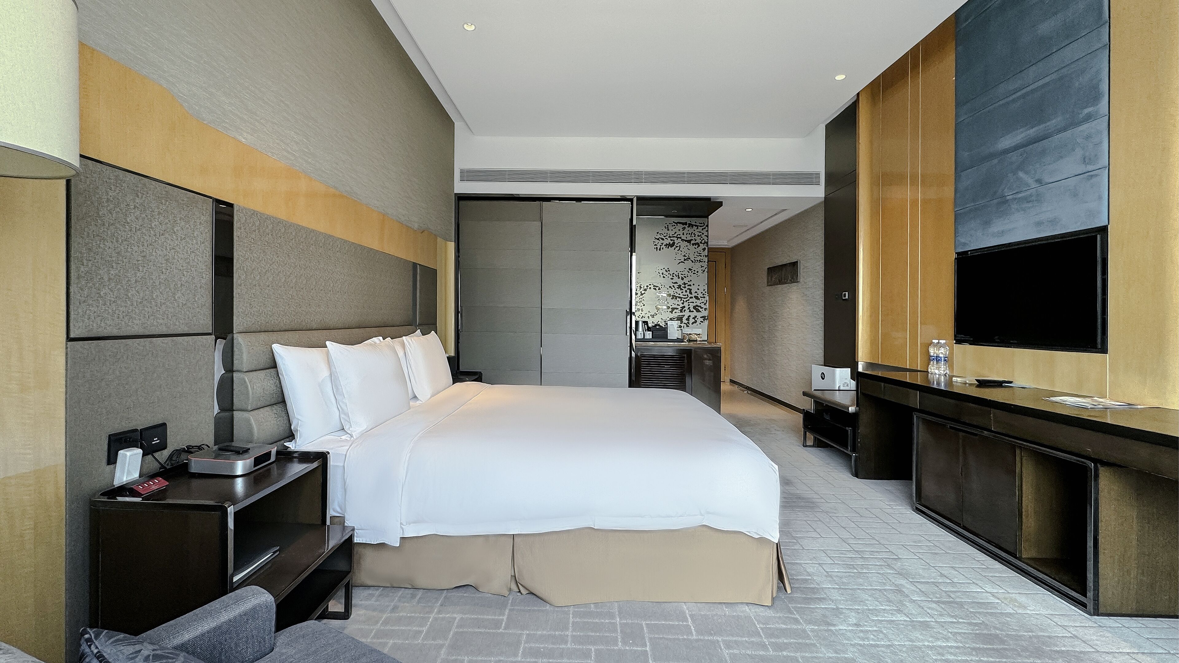 Ein modernes Hotelzimmer mit einem großen Bett, einem Schreibtisch mit Flachbildfernseher und einer Minibar.