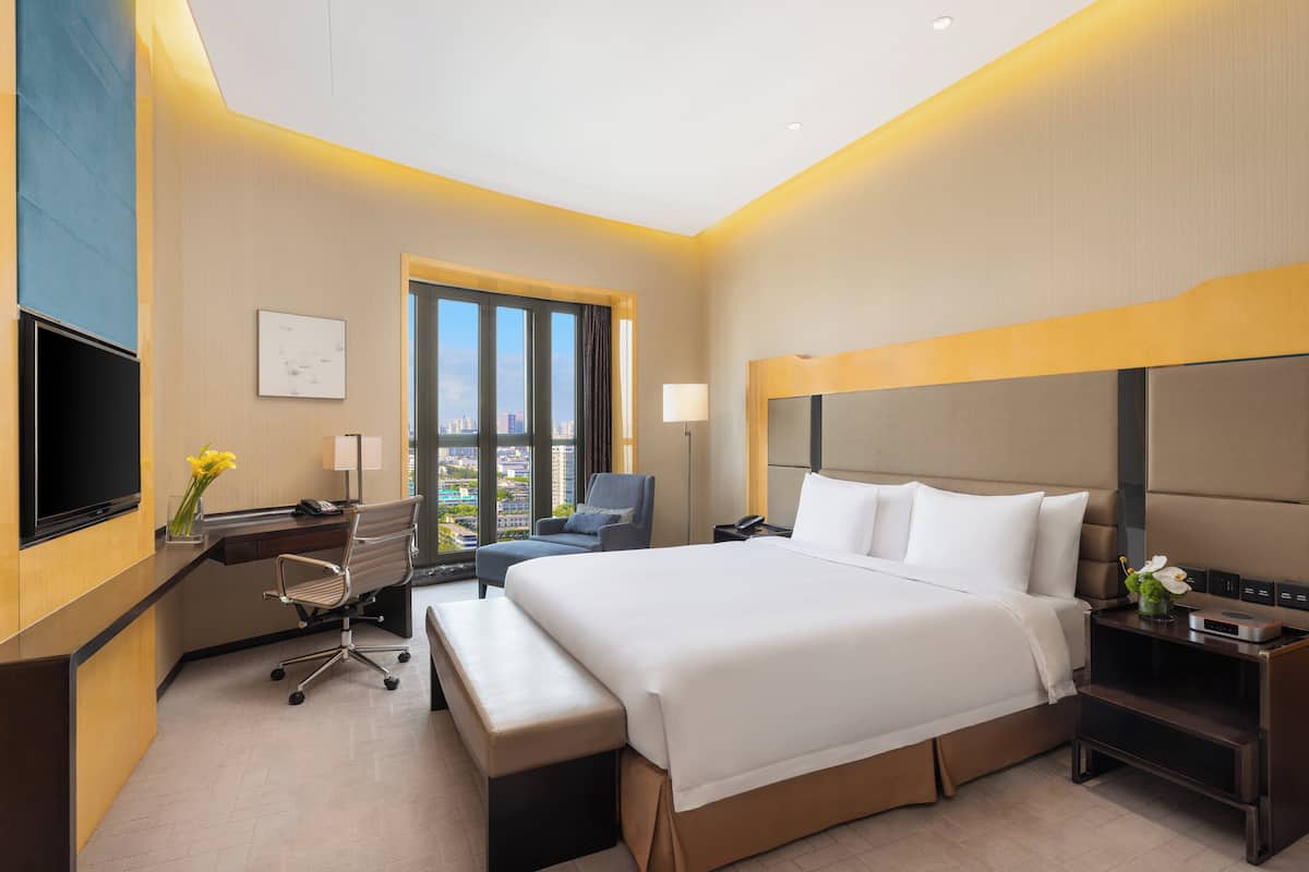Une chambre d’hôtel moderne dotée d’un grand lit, d’un bureau avec une chaise, d’une télévision et d’une fenêtre donnant sur la ville.