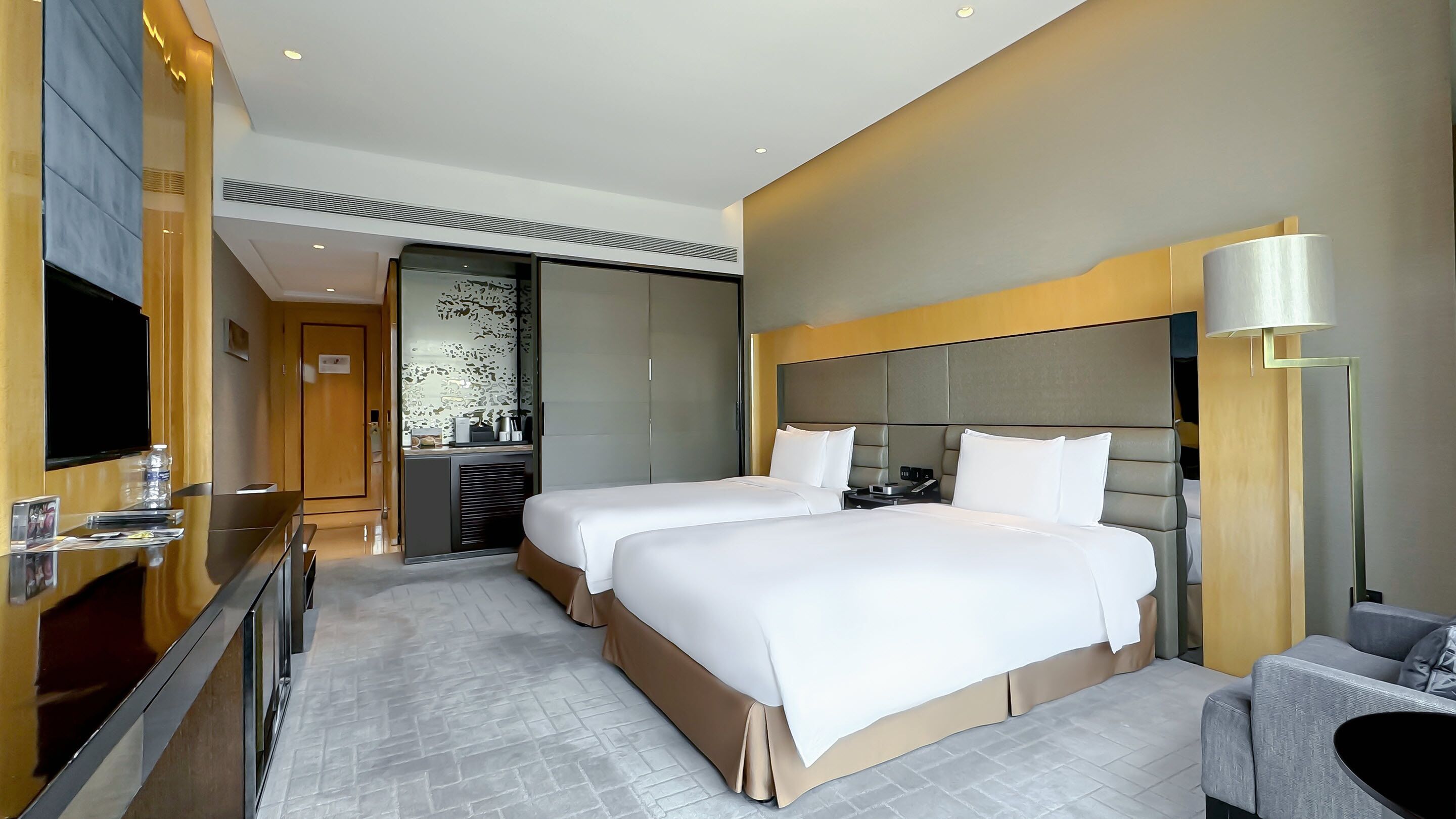 A hotel room with two beds, a TV, a desk with a lamp, and a modern design.
