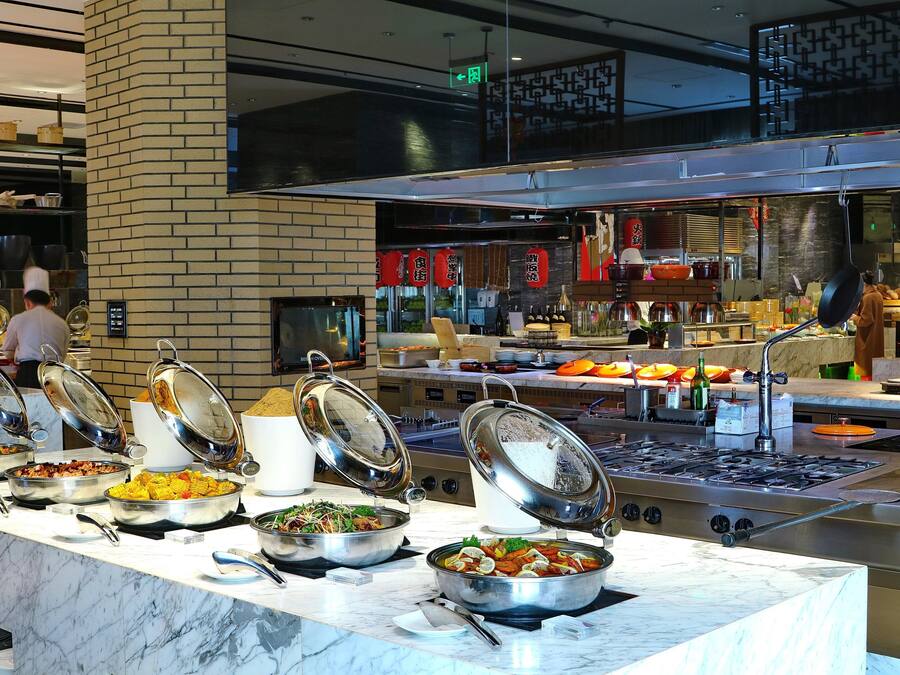 Een buffetopstelling met diverse gerechten en een moderne keuken op de achtergrond.