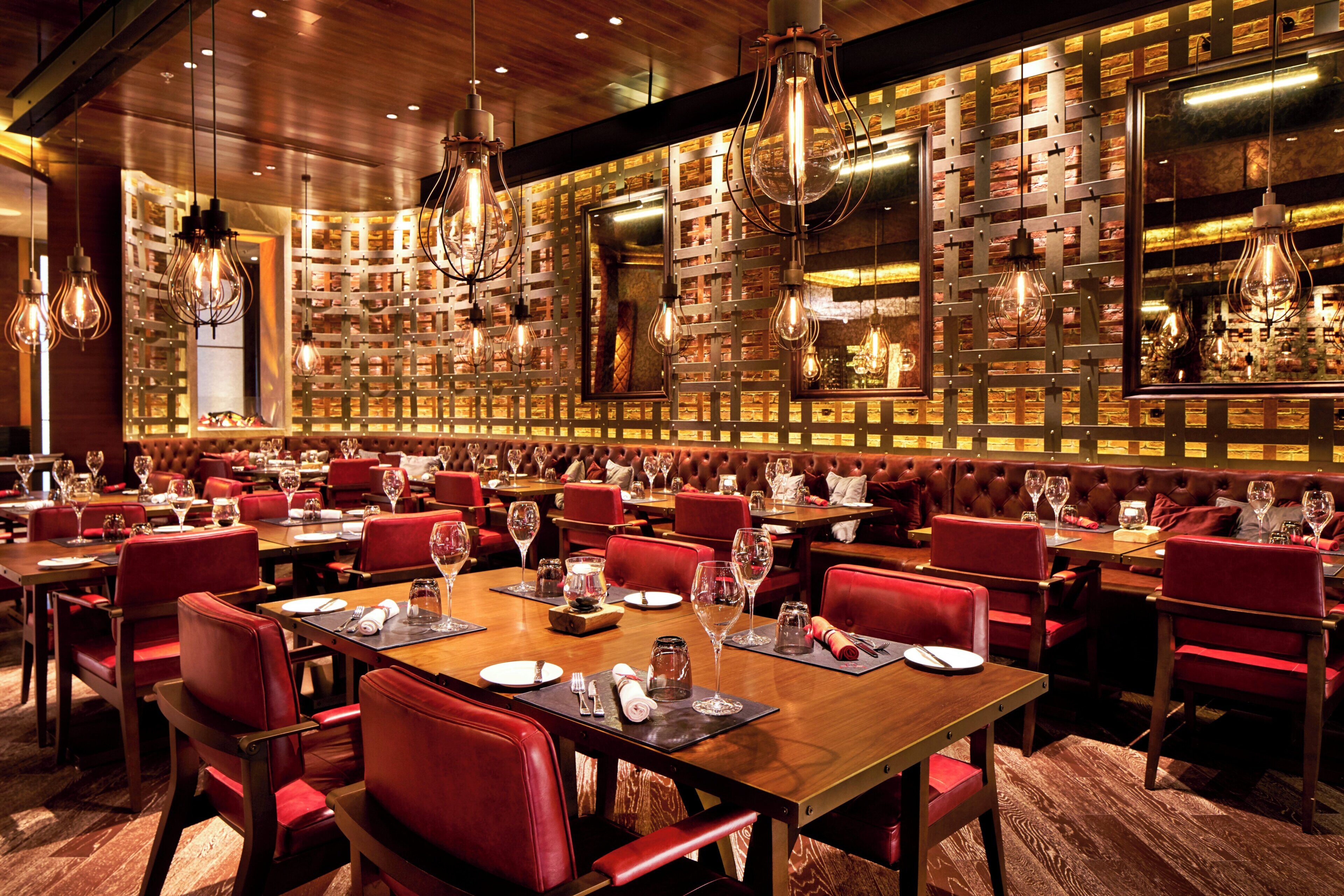 A restaurant interior with multiple dining tables, red upholstered booths, and hanging light fixtures.