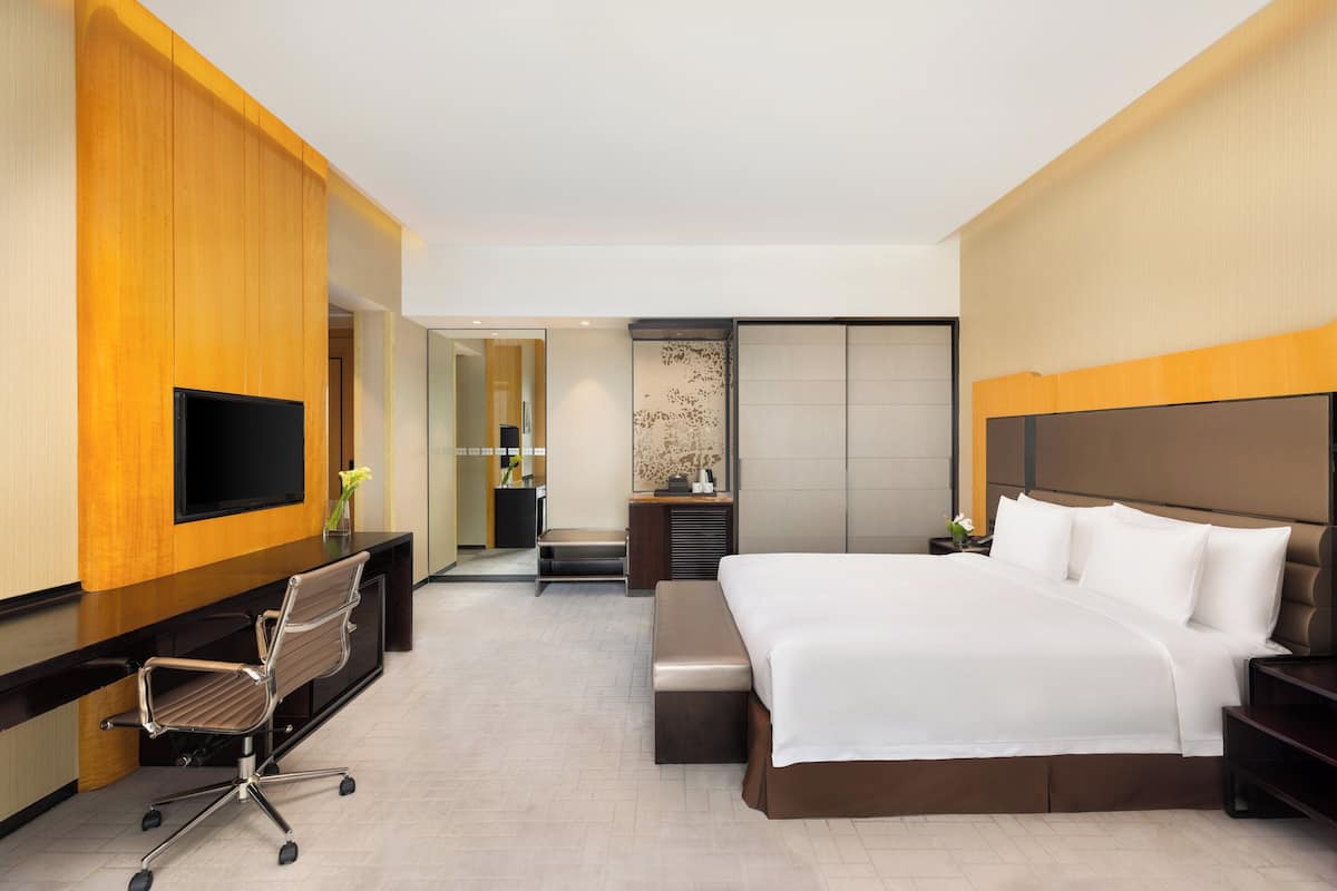 Une chambre d’hôtel moderne dotée d’un grand lit, d’un bureau avec un téléviseur à écran plat, d’une chaise et d’un banc.