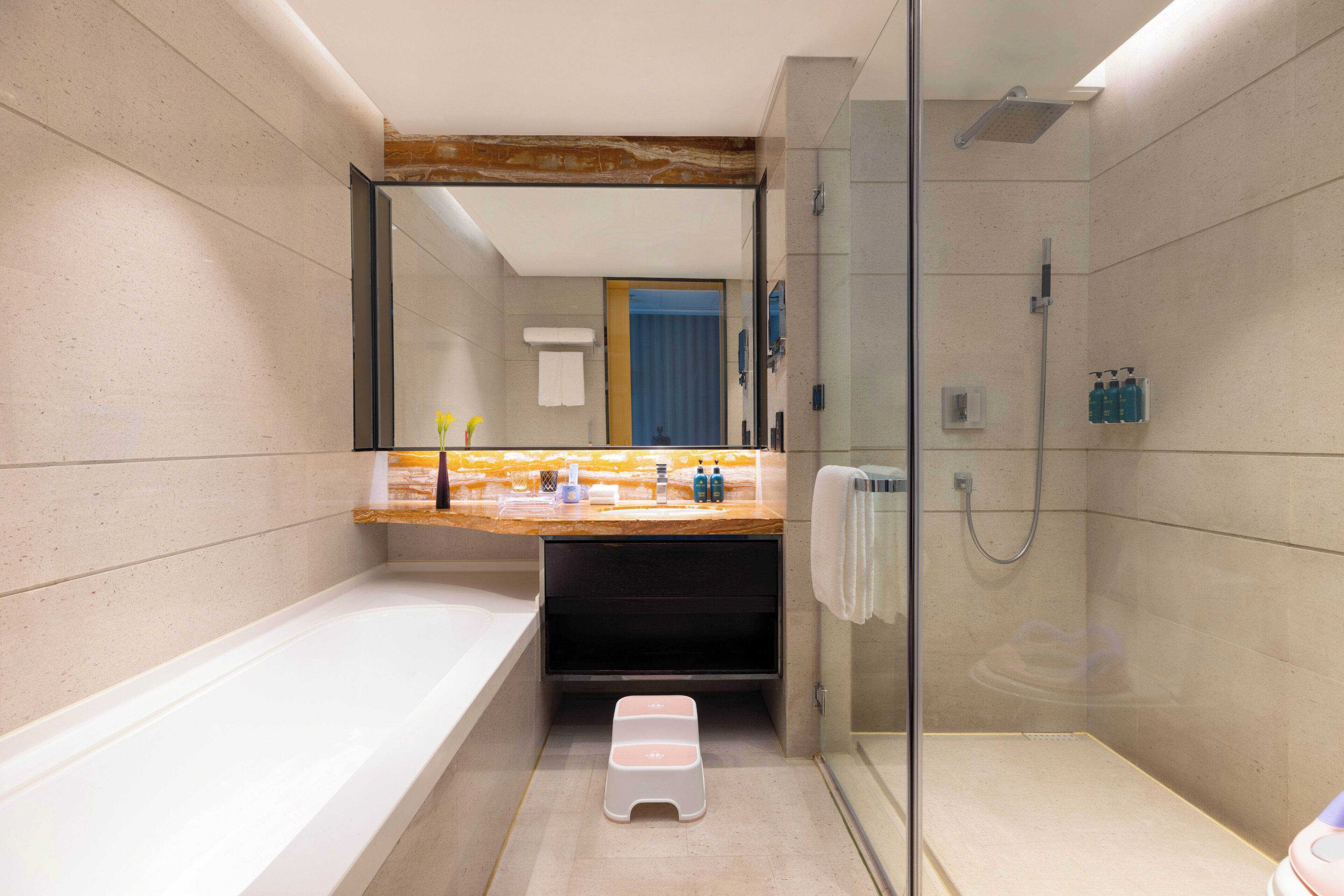 Un baño moderno con bañera, ducha con mampara de vidrio y tocador con artículos de aseo.