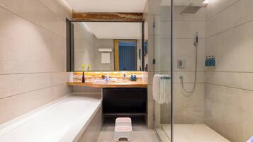 Un baño moderno con bañera, ducha con mampara de vidrio y tocador con artículos de aseo.
