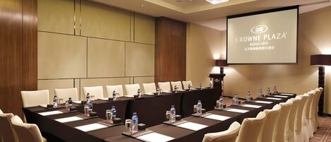 A conference room with a long table, multiple chairs, water bottles, and a projector screen displaying "Crowne Plaza Beijing Lido".