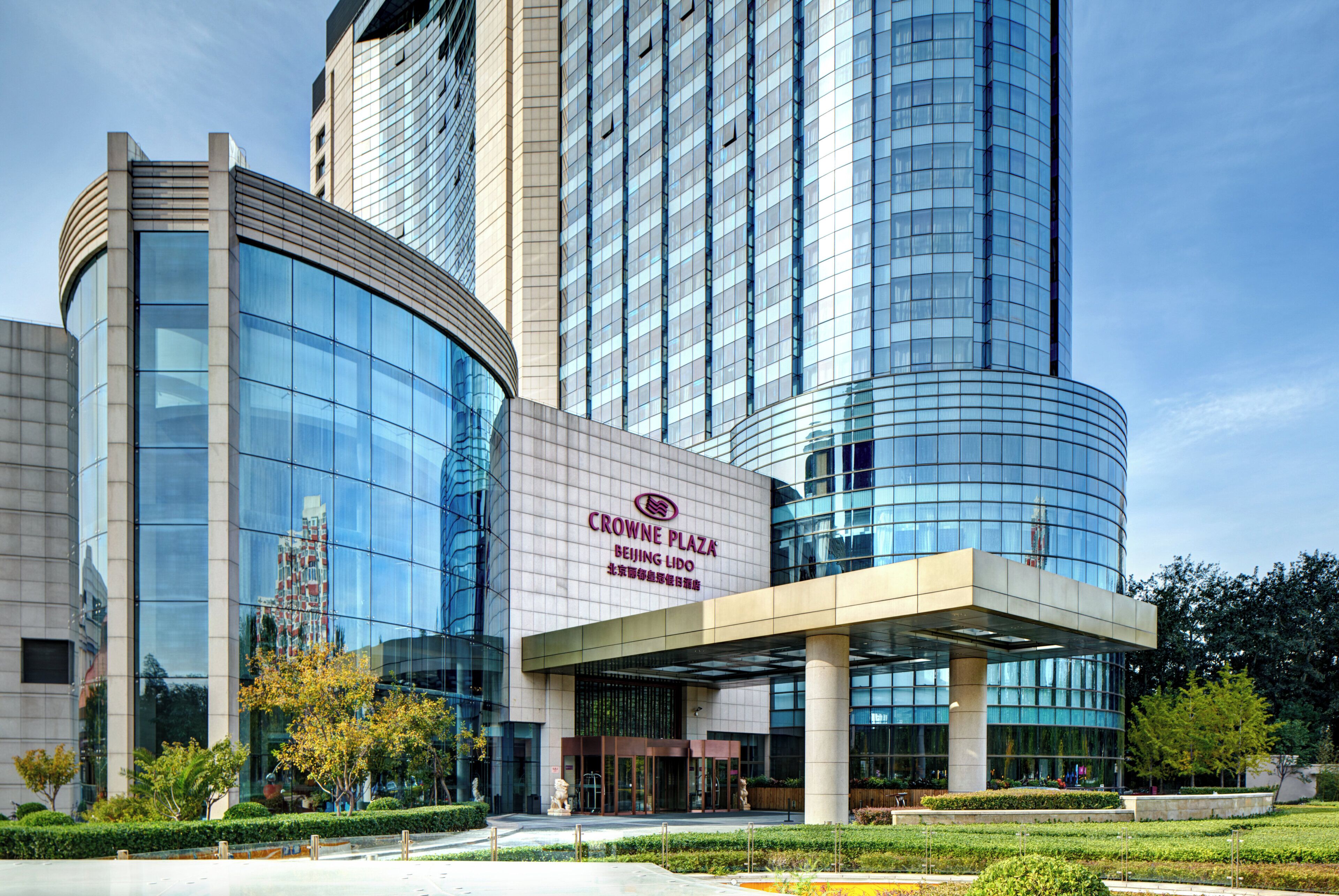 A modern building with a curved glass facade and a sign reading 'CROWNE PLAZA BEIJING LIDO'.
