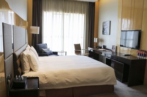 A hotel room with a large bed, a desk, a chair, a TV, and a window with curtains.