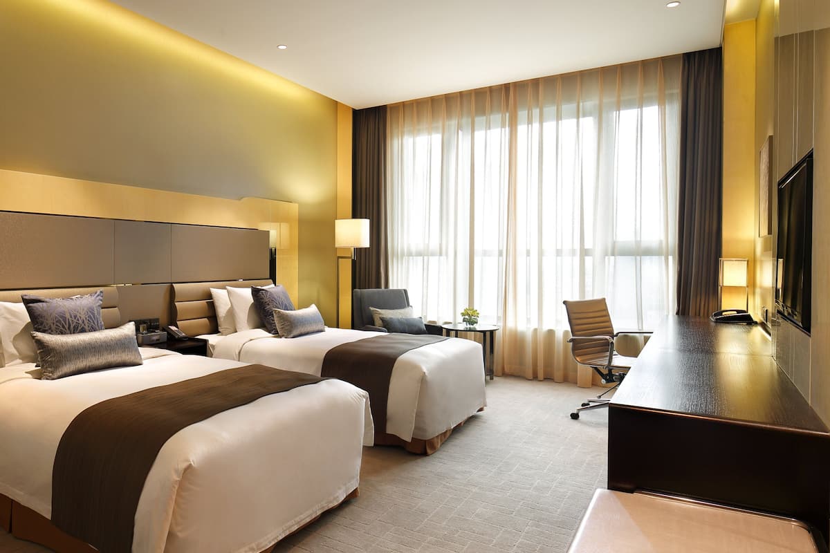 Une chambre d’hôtel avec deux lits, un bureau et une télévision.