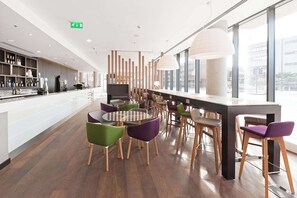 A modern bar area with a long counter, multiple stools, and a round table with chairs.