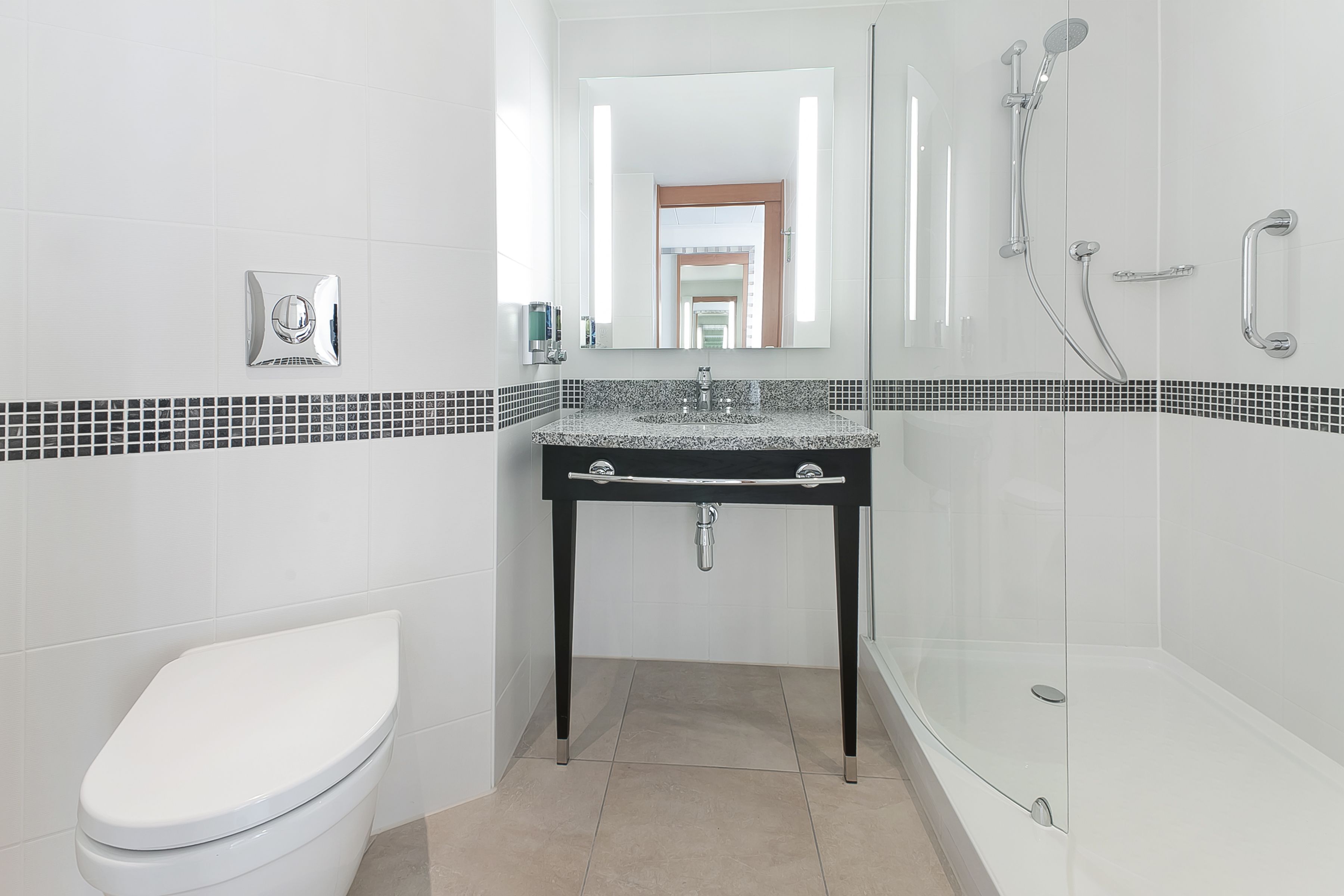 Un baño moderno con inodoro blanco, lavamanos con espejo y zona de ducha con mampara de vidrio.