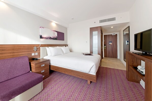 Una habitación de hotel con una cama, un sofá morado, un televisor y una pintura de un paisaje urbano en la pared.