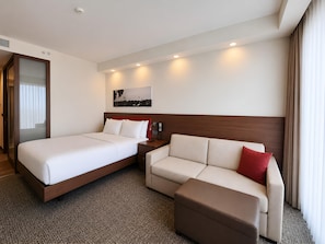 Una habitación de hotel con cama, sofá, una mesita y teléfono en la pared.