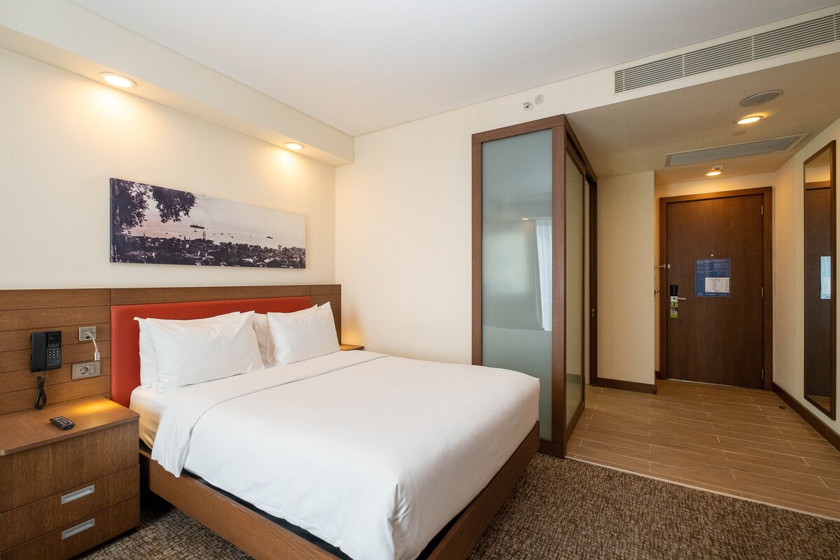 Una habitación de hotel con cama, mesita de noche y un cuadro en la pared.