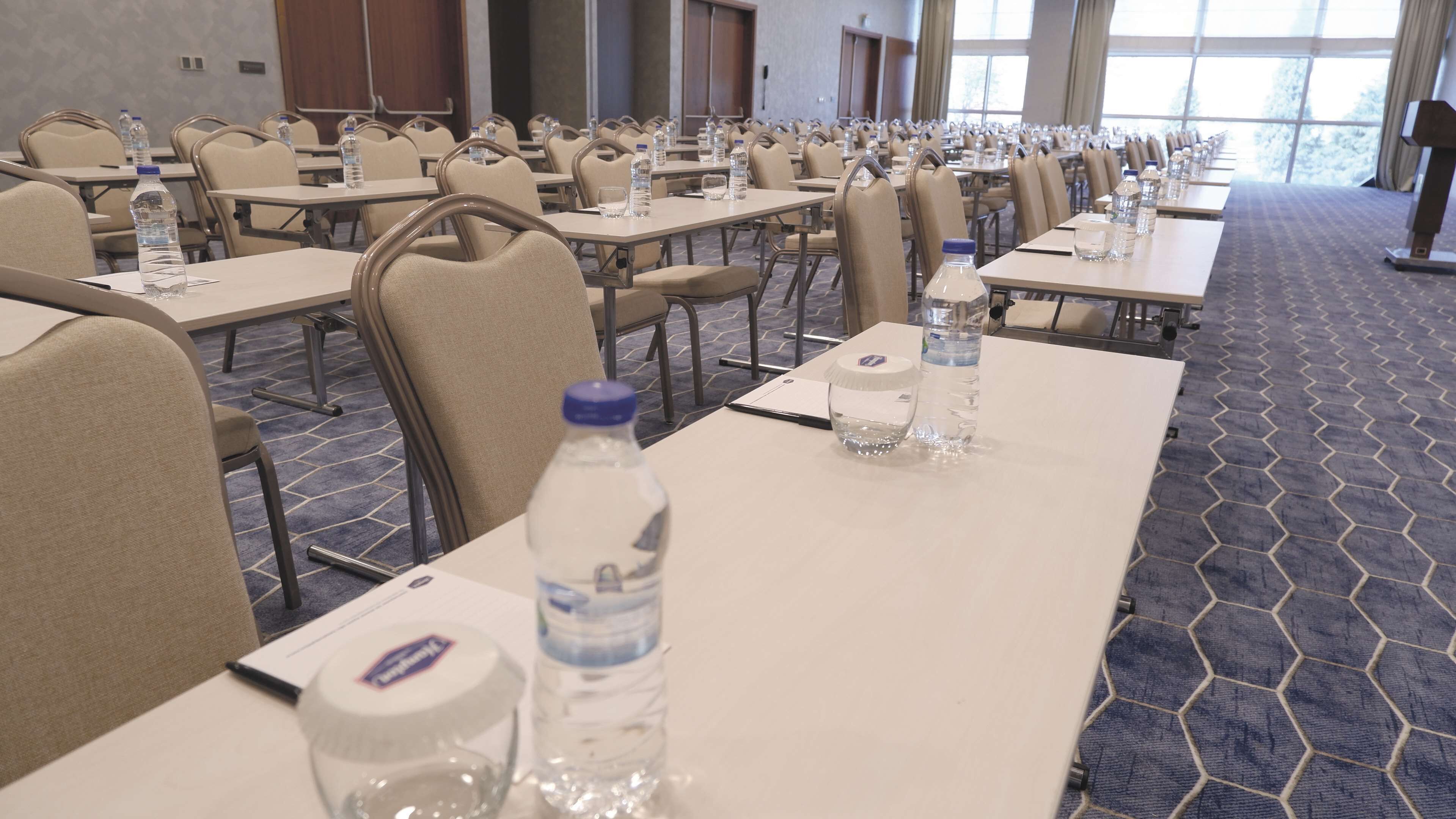 Un salón de conferencias con filas de mesas, sillas, botellas de agua y tarjetas de identificación.