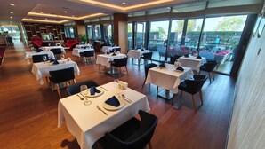 Un restaurante con varias mesas, manteles blancos, sillas negras y vistas al exterior.