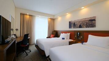 A hotel room with two beds, a desk, a chair, a TV, and a painting on the wall.