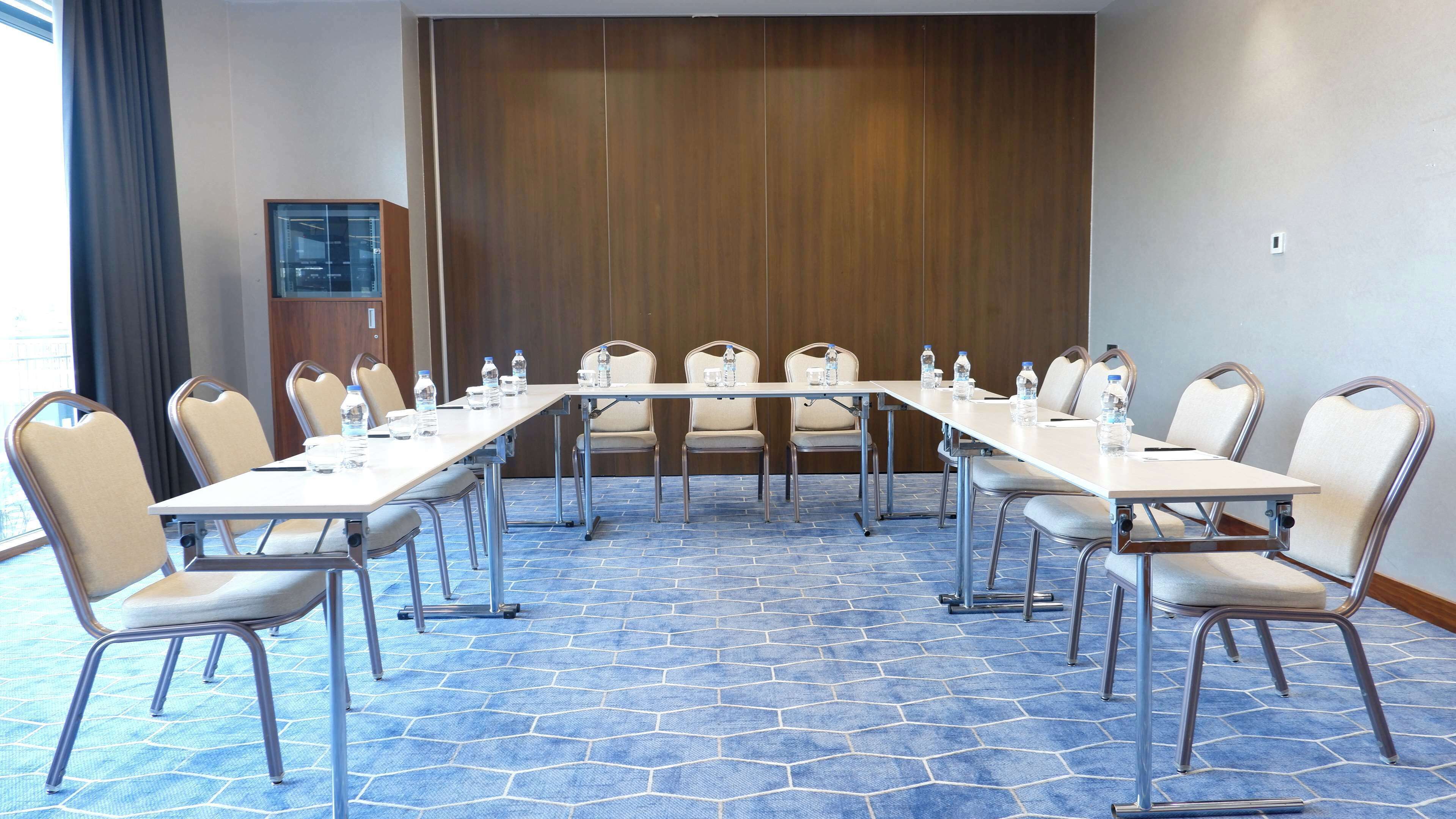 A conference room with a long table, chairs, water bottles, and a wooden panel wall.