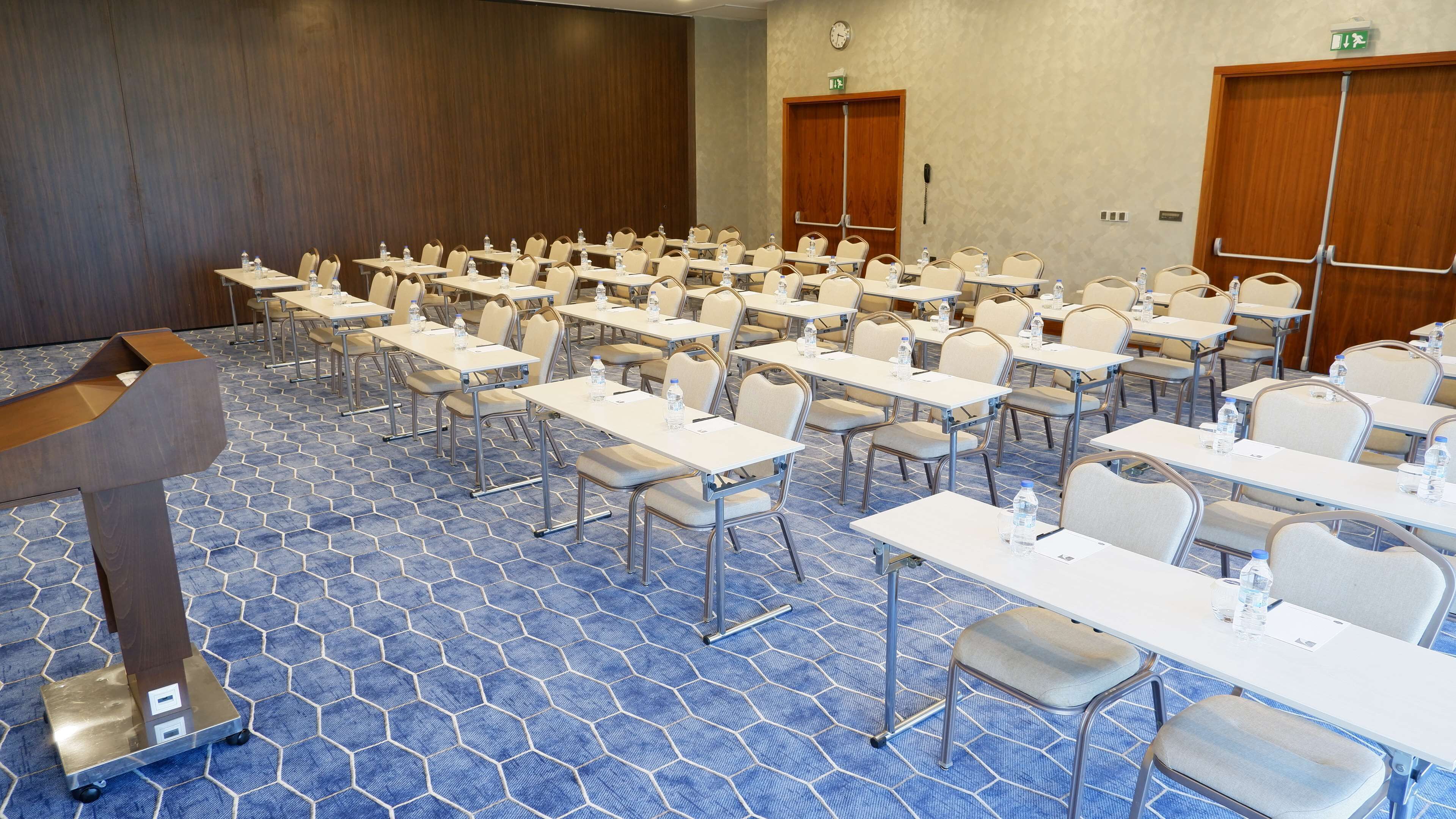 A conference room with rows of tables and chairs, a podium, and a patterned carpet.