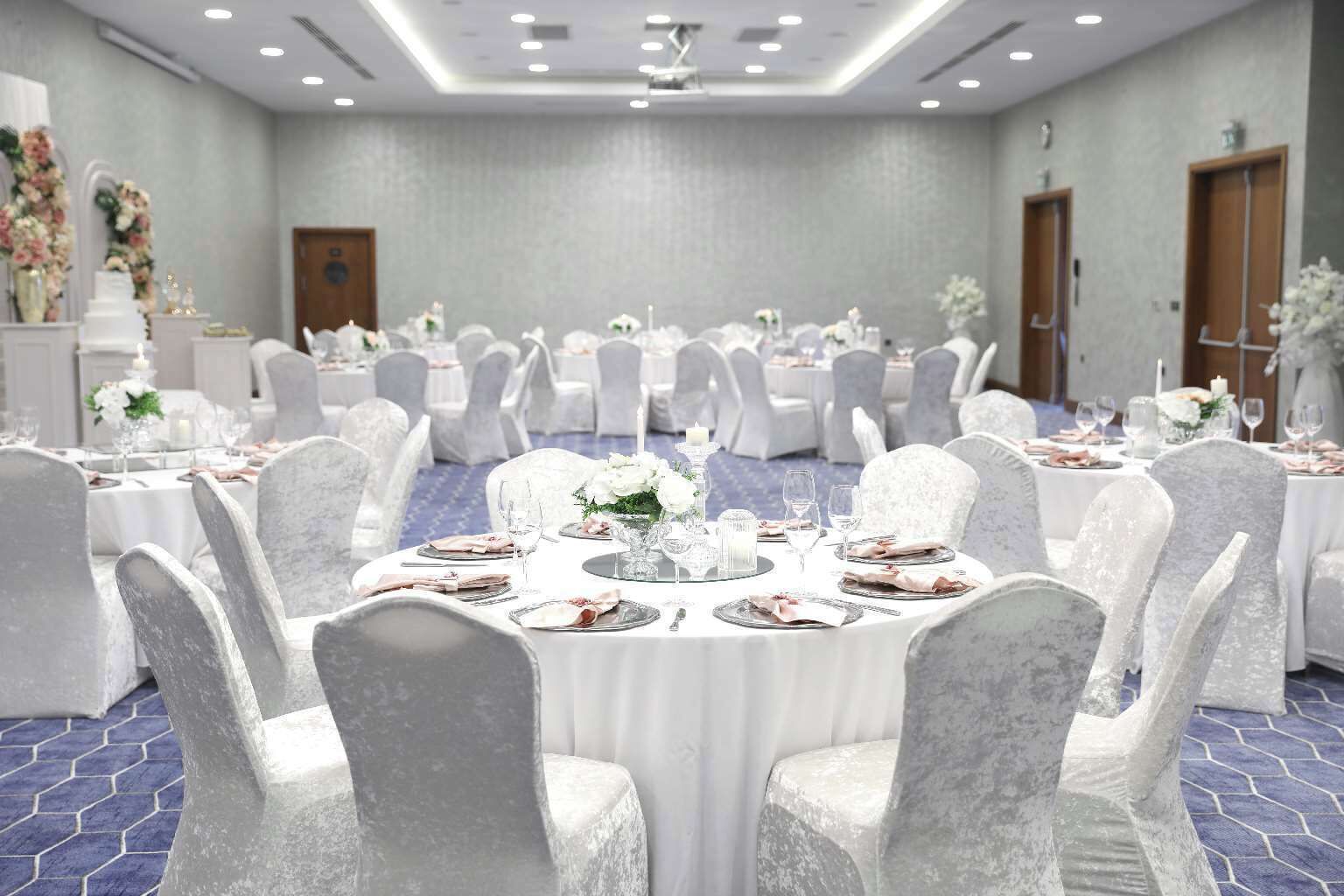 A banquet hall with round tables, white tablecloths, and chairs with white covers.