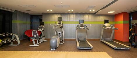 Un gimnasio con cintas de correr, máquinas elípticas y una banca para pesas.