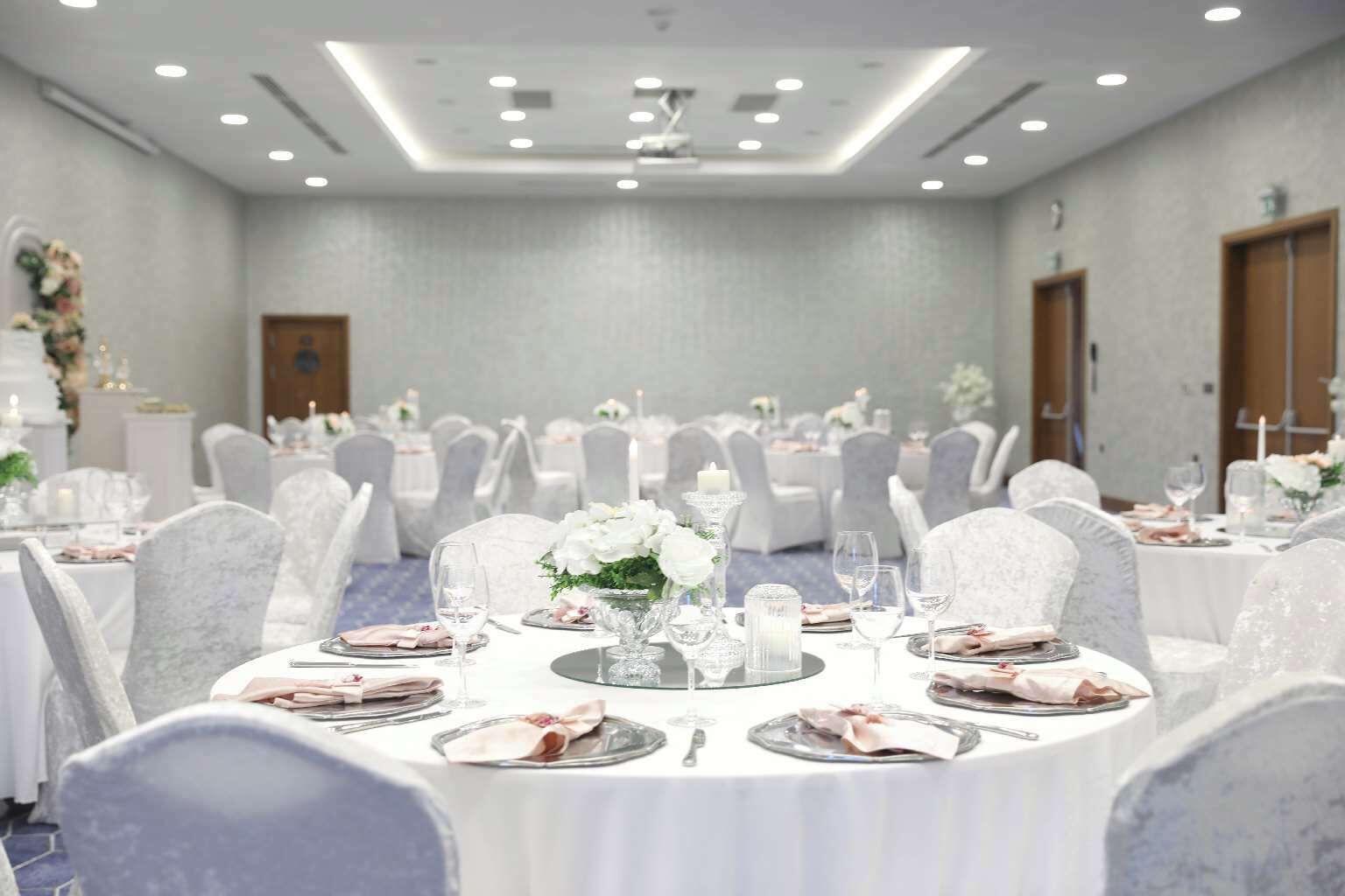 A banquet hall with round tables set for dining, white chairs, and floral centerpieces.