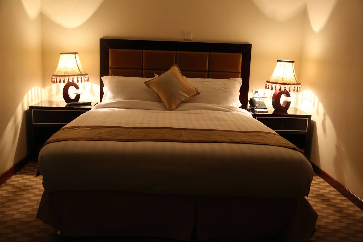 A hotel room with a large bed, two bedside lamps, and a nightstand with a telephone.