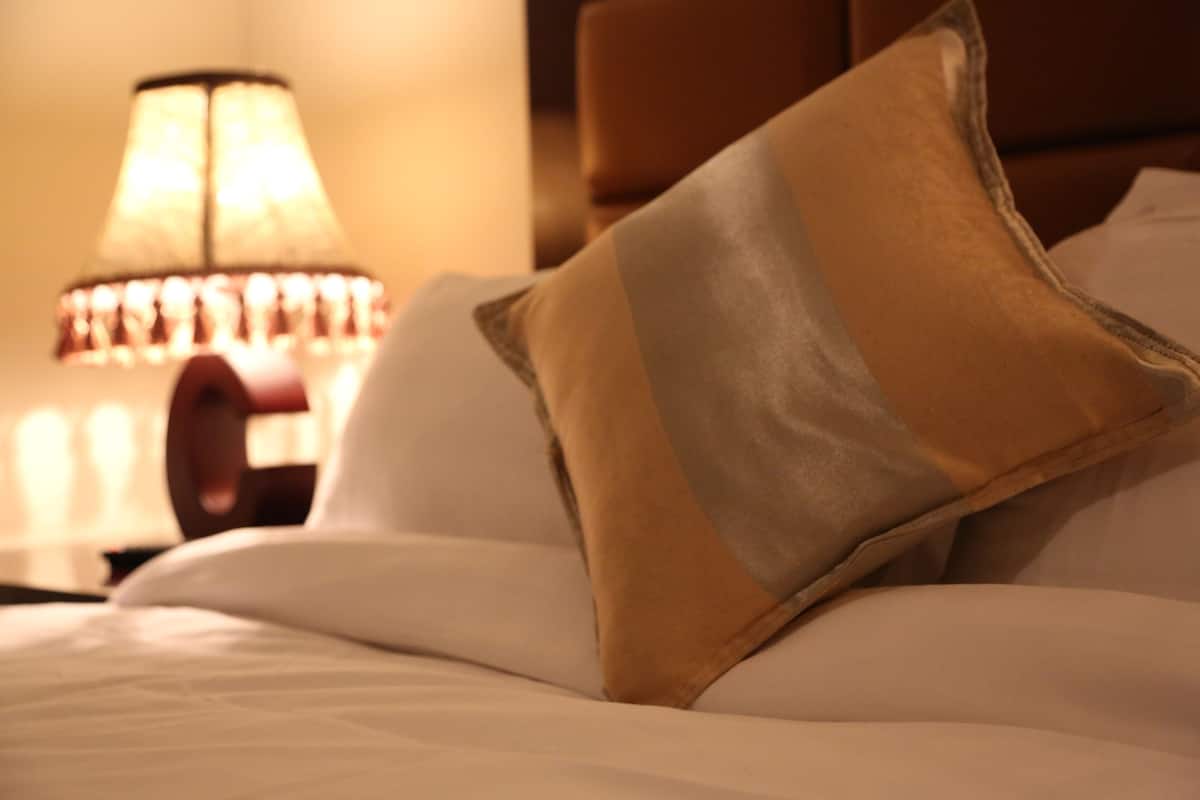 A bed with white bedding and a single decorative pillow.