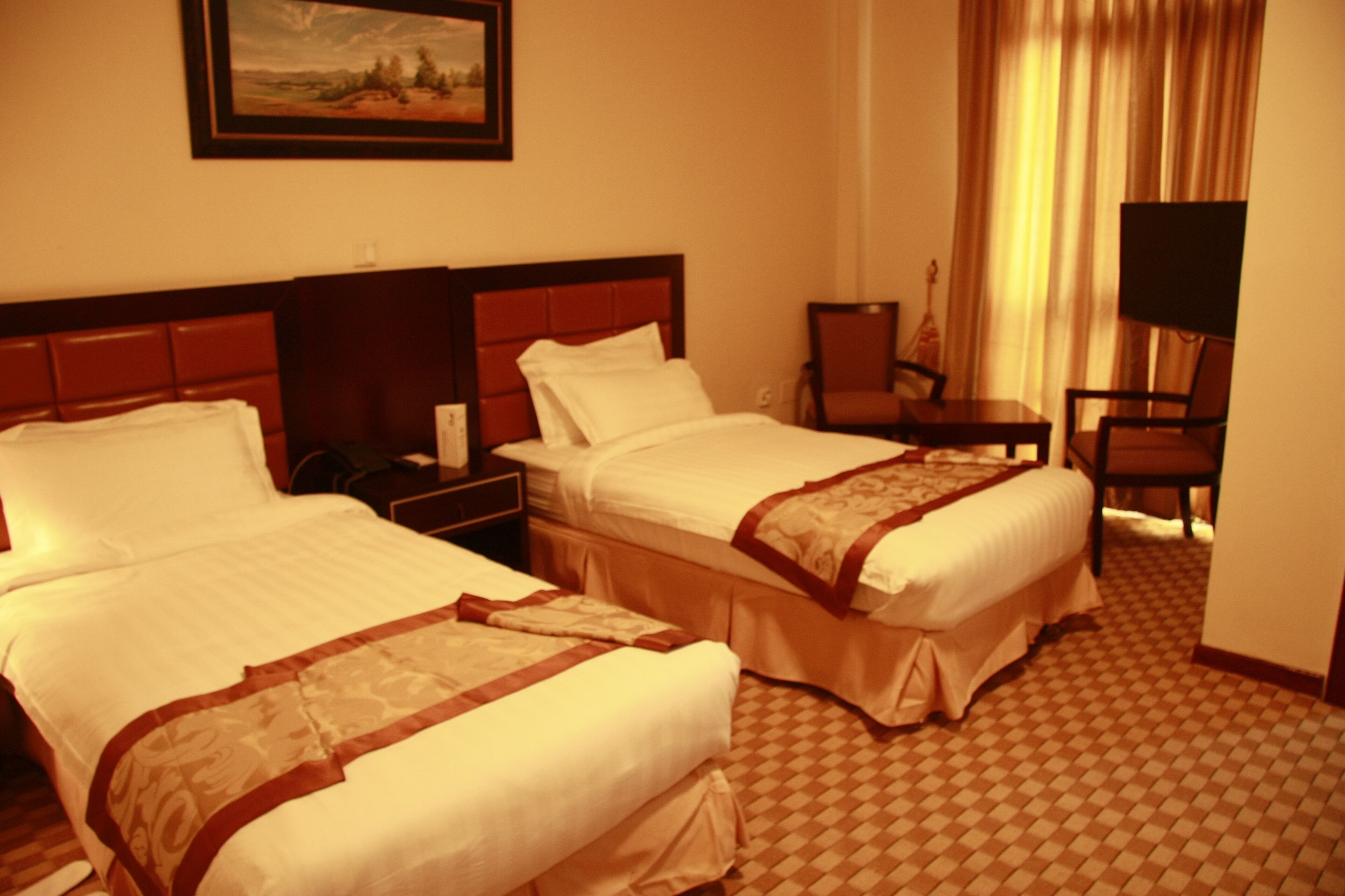 A hotel room with two beds, a desk, a chair, and a television.