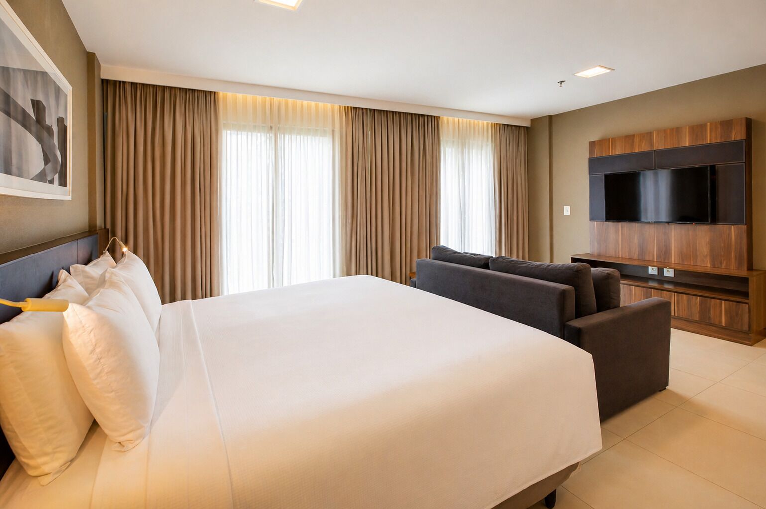 Une chambre d’hôtel avec un grand lit, un canapé, un téléviseur à écran plat et un tableau au mur.