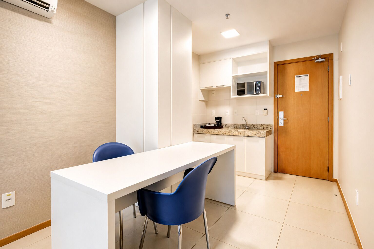 A modern kitchen with white cabinets, a countertop, and a built-in oven. There is a wooden door with a handle and a small window.