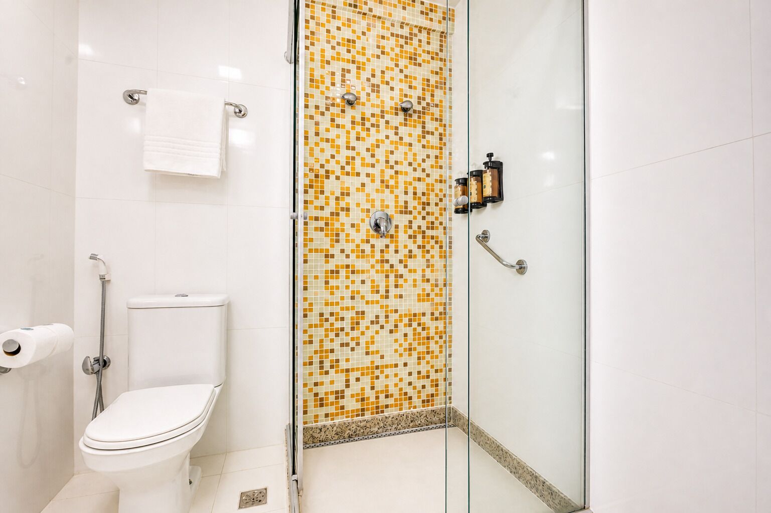 Une salle de bain comprenant des toilettes, une douche avec un mur recouvert de mosaïques et une porte de douche en verre.